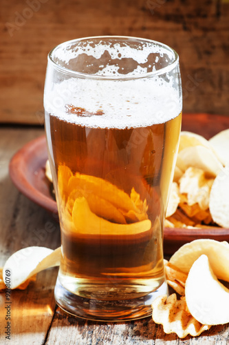 large glass of light beer and potato chips on a wooden backgroun