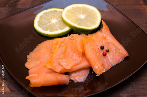 Smoked salmon on black plate on wooden table seen close