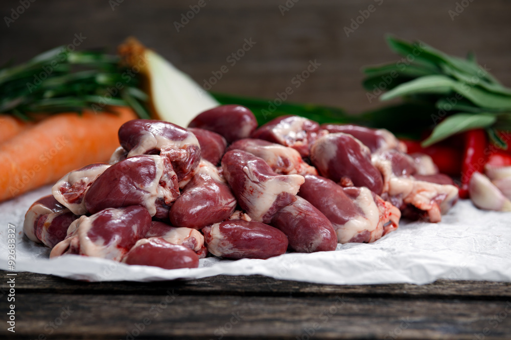 Raw Duck hearts on crumpled paper, decorated with vegetables. on old wooden table