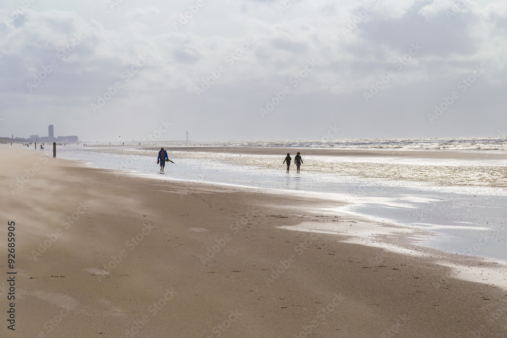 People walking along the beach against strong winds carrying sand at North Sea coast, Belgium
