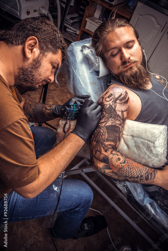 Fototapeta premium Professional tattooer showing process of making a tattoo in tattoo parlor