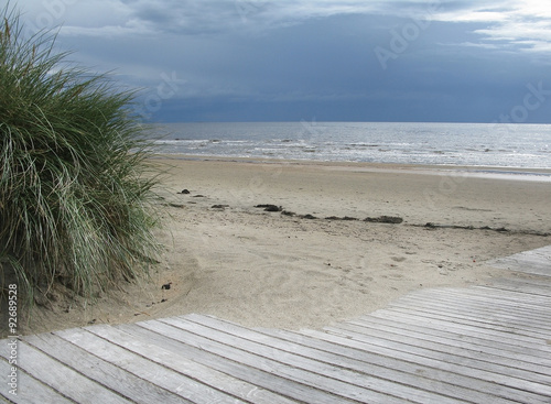 Sand dune landscape with wooden boardwalk leading towards sea and sky at Skrea Strand on a sunny day with dark clouds in Falkenberg, Sweden. photo