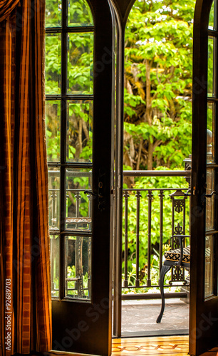 Open French doors onto a balcony with a view of leafy green trees