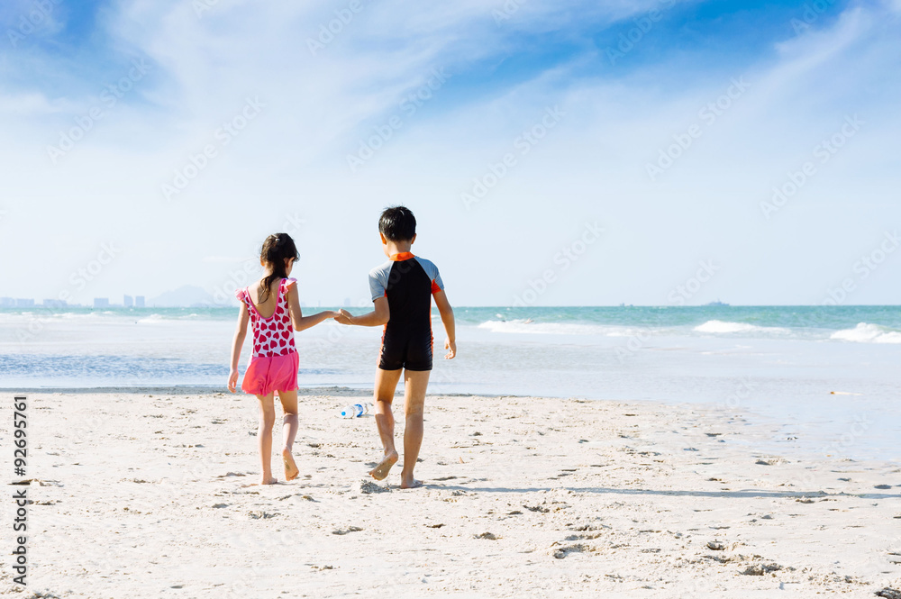 Brother sister holding hand walk on the beach to colleact bottle