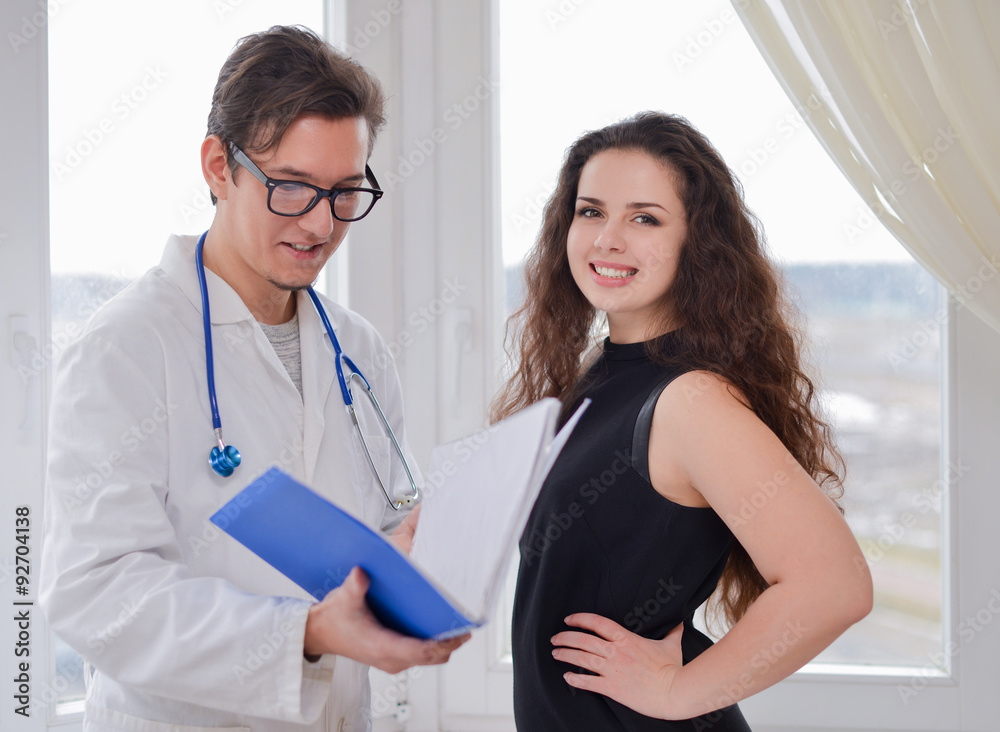 Fototapeta premium Male doctor with folder and patient standing near window at hospital