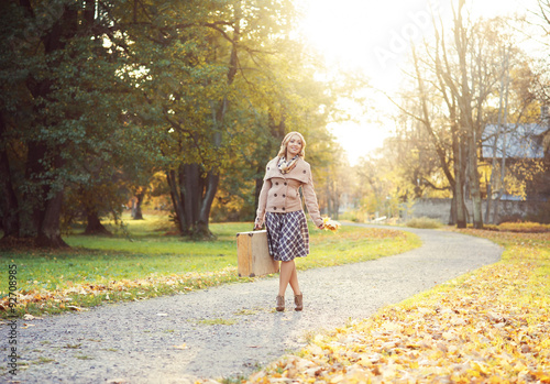 Attractive young woman walking with a bouquet of autumn leaves and a suitcase. © Acronym