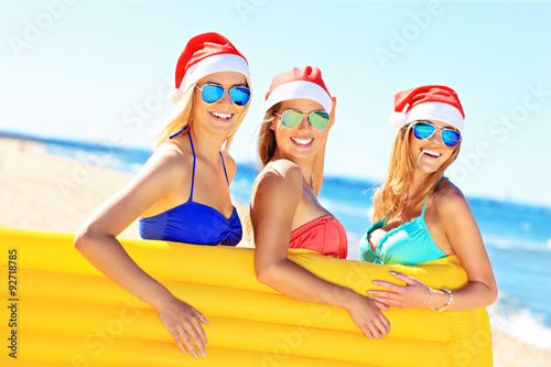 Group of girls in Santa's hats having fun on the beach