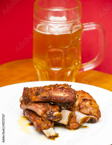 Roasted pork ribs on a white plate with a pitcher of beer next