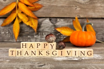 Happy Thanksgiving wooden blocks against a rustic wood background with pumpkins and autumn leaves