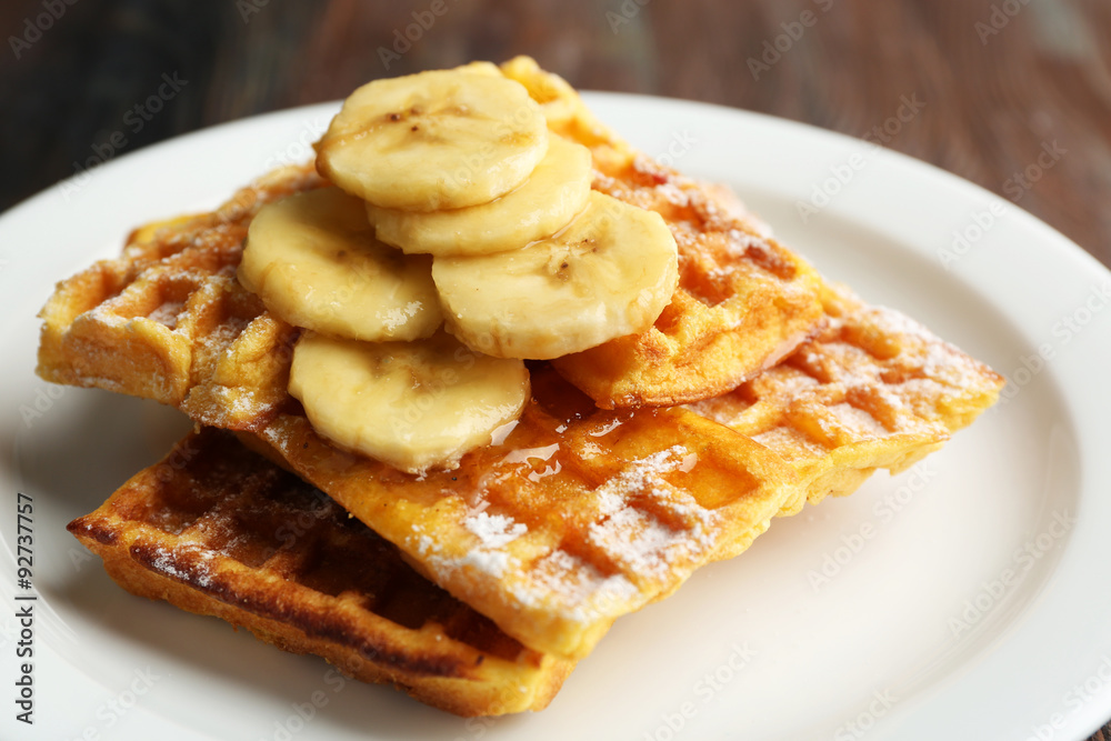 Sweet homemade waffles with sliced banana on plate, on light background Sweet homemade waffles with sliced banana on plate, on light background