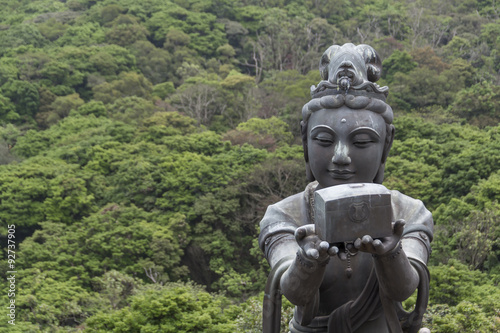 Buddhistic statue making offerings to the Tian Tan Buddha in Hong Kong, against a background of lush trees
