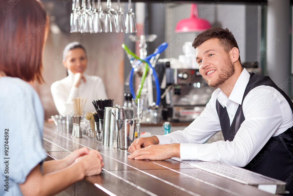 Attractive young barman is flirting with female customers Attractive young barman is flirting with female customers
