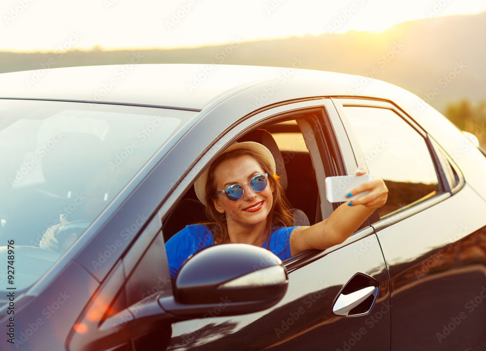 Naklejka premium Young woman in hat and sunglasses making self portrait sitting i