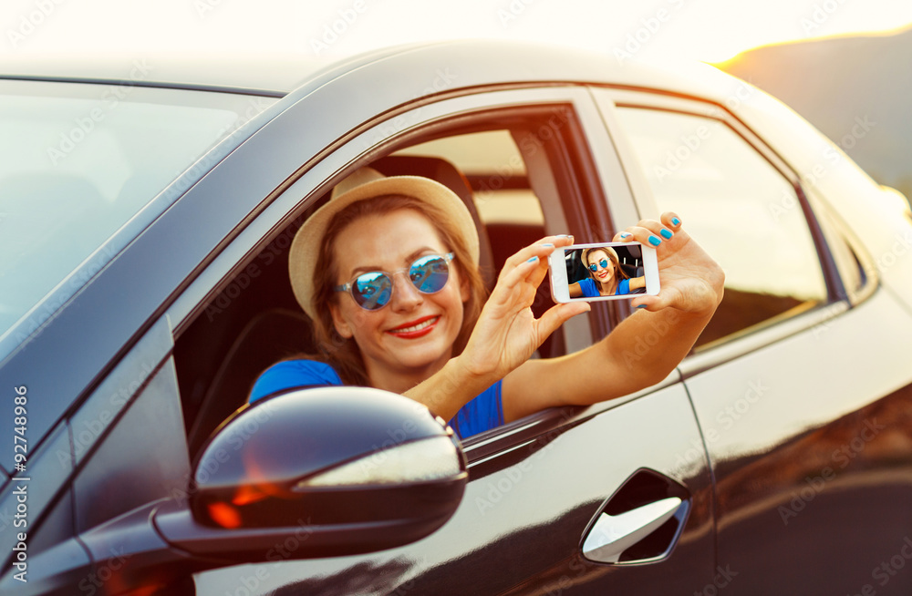 Naklejka premium Young woman in hat and sunglasses making self portrait sitting i