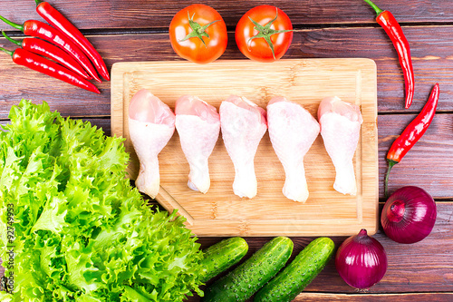 Chicken legs and vegetables on an old table: tomatoes, cucumbers, pepper, onions, lettuce leaves photo