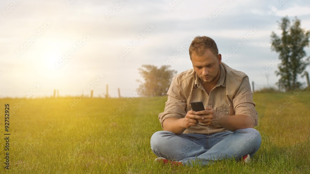 Handsome young man talking on smart phone at sunset outdoors. Using smartphone for a phone call, smiling happy wearing urban hipster outfit outdoors in peaceful autumn nature Handsome young man talking on smart phone at sunset outdoors. Using smartphone for a phone call, smiling happy wearing urban hipster outfit outdoors in peaceful autumn nature