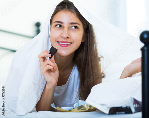 Happy girl hiding under sheet with sweets indoors