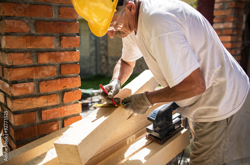 Obraz na plátně Senior man finishing wooden beam with sander