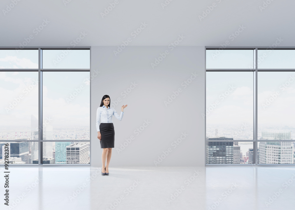 Full length brunette girl in a formal clothes is pointing out something by her hand on the white wall. A modern panoramic office in Manhattan, New York. Full length brunette girl in a formal clothes is pointing out something by her hand on the white wall. A modern panoramic office in Manhattan, New York.