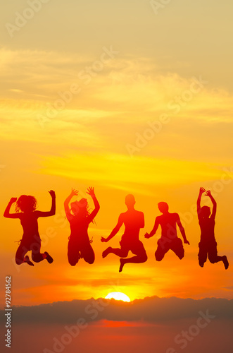 Teenage boys and girls jumping high in the air against colorful sunset