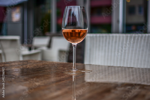 Close-up of a glass of rose wine on the brown table. Photographed on a rainy day. The table is wet.