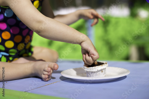 Renkli puantiyeli mayo giymiş küçük bebek çikolatalı keki parmakları ile yemeye çalışıyor. photo