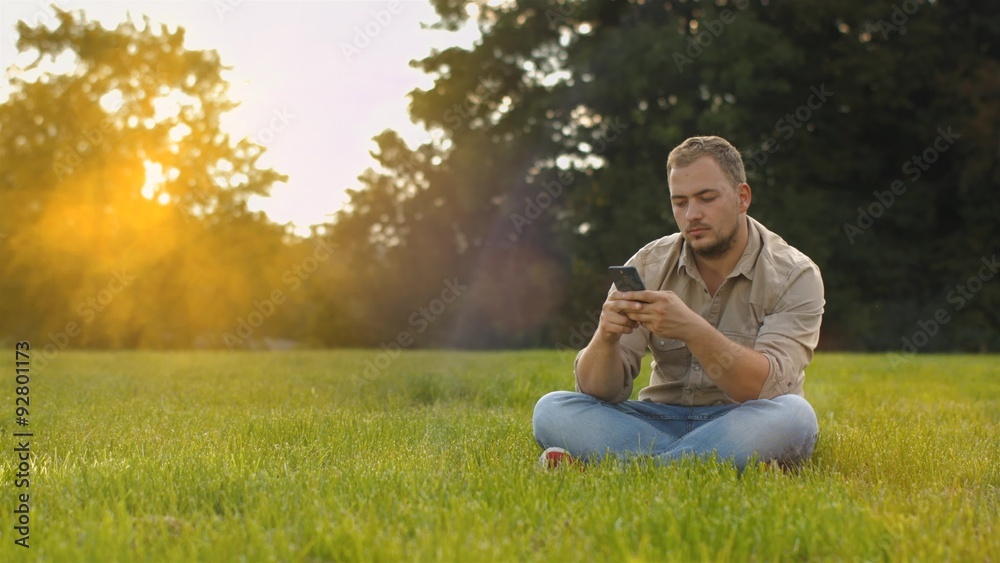 Handsome young man talking on smart phone at sunset outdoors. Using smartphone for a phone call, smiling happy wearing urban hipster outfit outdoors in peaceful autumn nature Handsome young man talking on smart phone at sunset outdoors. Using smartphone for a phone call, smiling happy wearing urban hipster outfit outdoors in peaceful autumn nature