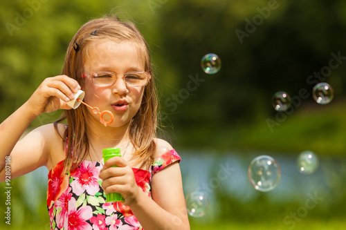 Little girl child blowing soap bubbles outdoor.