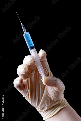 hand with surgical glove and syringe for injection on black background