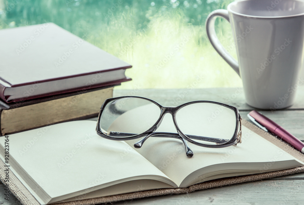 Fototapeta premium eyeglasses on open notebook with book,pen and coffee cup 