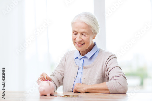 senior woman putting money to piggy bank at home