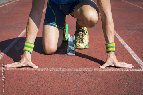 Athlete crouching at the starting line of a running track with gold shoe feet in sprinter starting blocks