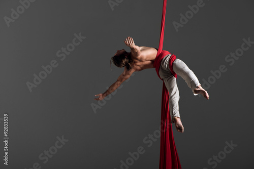 Sporty young man doing exercise with elastics, aerial silk ribbons, aerial. Sport training gym and lifestyle concept. Anti-gravity yoga.