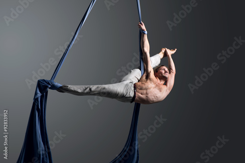 Sporty young man doing exercise with elastics, aerial silk ribbons, aerial. Sport training gym and lifestyle concept. Anti-gravity yoga. photo