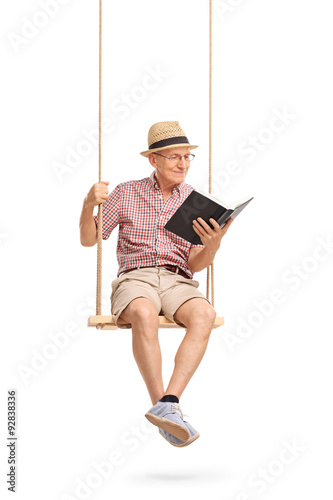 Joyful senior sitting on swing and reading a book