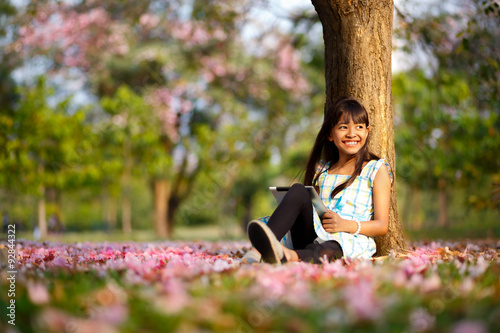 Happy asian girl sitting on grass with tablet computer in the park