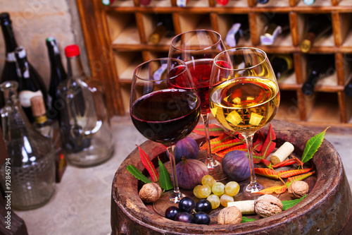 Red, rose and white glasses and bottles of wine. Grape, fig, nuts and leaves on old wooden barrel