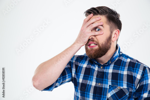 Man covering his face with palm and looking at camera through fingers