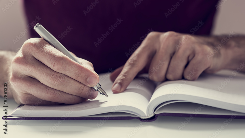 Male student writing notes with fountain pen in his notebook - obrazy, fototapety, plakaty 