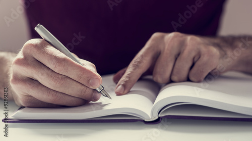 Male student writing notes with fountain pen in his notebook photo