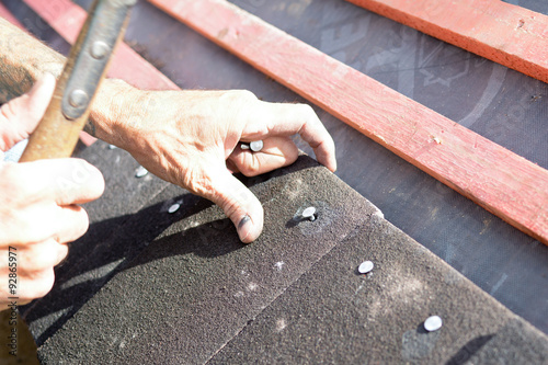 A roofer using hammer to nail tiles to wooden roof battens