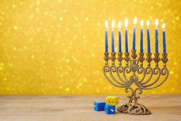 Jewish holiday Hanukkah background with vintage menorah and spining top dreidel over lights bokeh