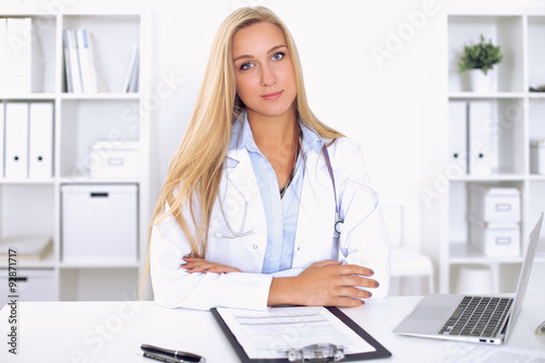 Blonde female doctor sitting at the table in hospital
