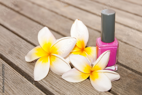 Fuchsia nail polish in the bottle and flowers on the woody background