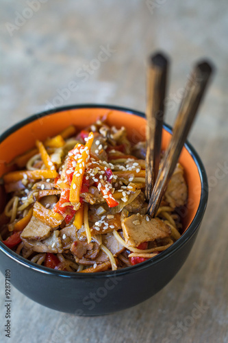 Fotografija Stir fry with vegetables and meat garnished with sesame seeds in bowl with chopsticks