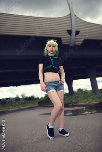 Beautiful young swag woman with green hair posing near highway road