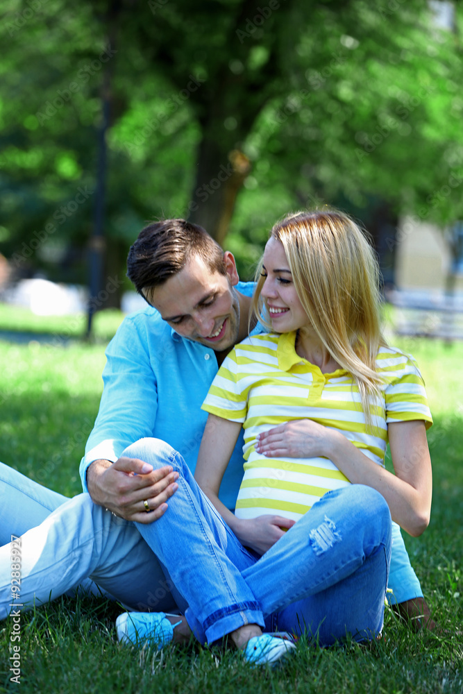 Fototapeta premium Young pregnant woman with husband sitting on green grass in park