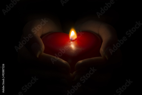 Woman's hands holding a burning wax red heart, isolated on black background