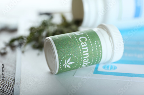 Bottle of dry medical cannabis with clipboard on table close up