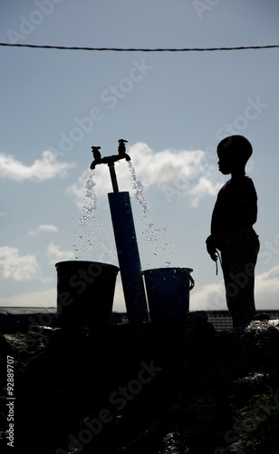 Fotografie Silhouette of a young boy gathering water at a well in Langa, South Africa, a township located on the outskirts of Cape Town